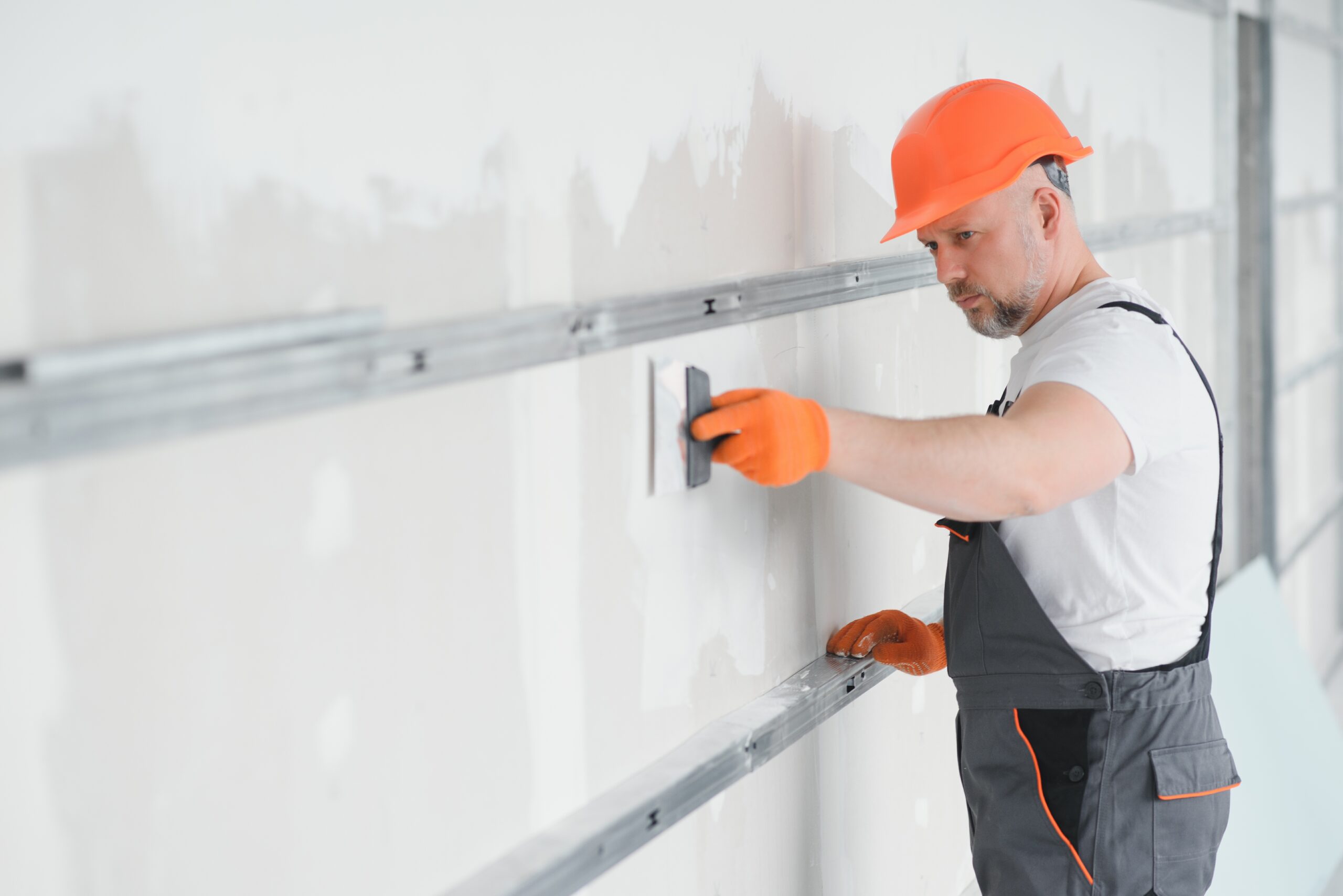 man drywall worker using trowel for plasterer putting stucco on plasterboard white wall