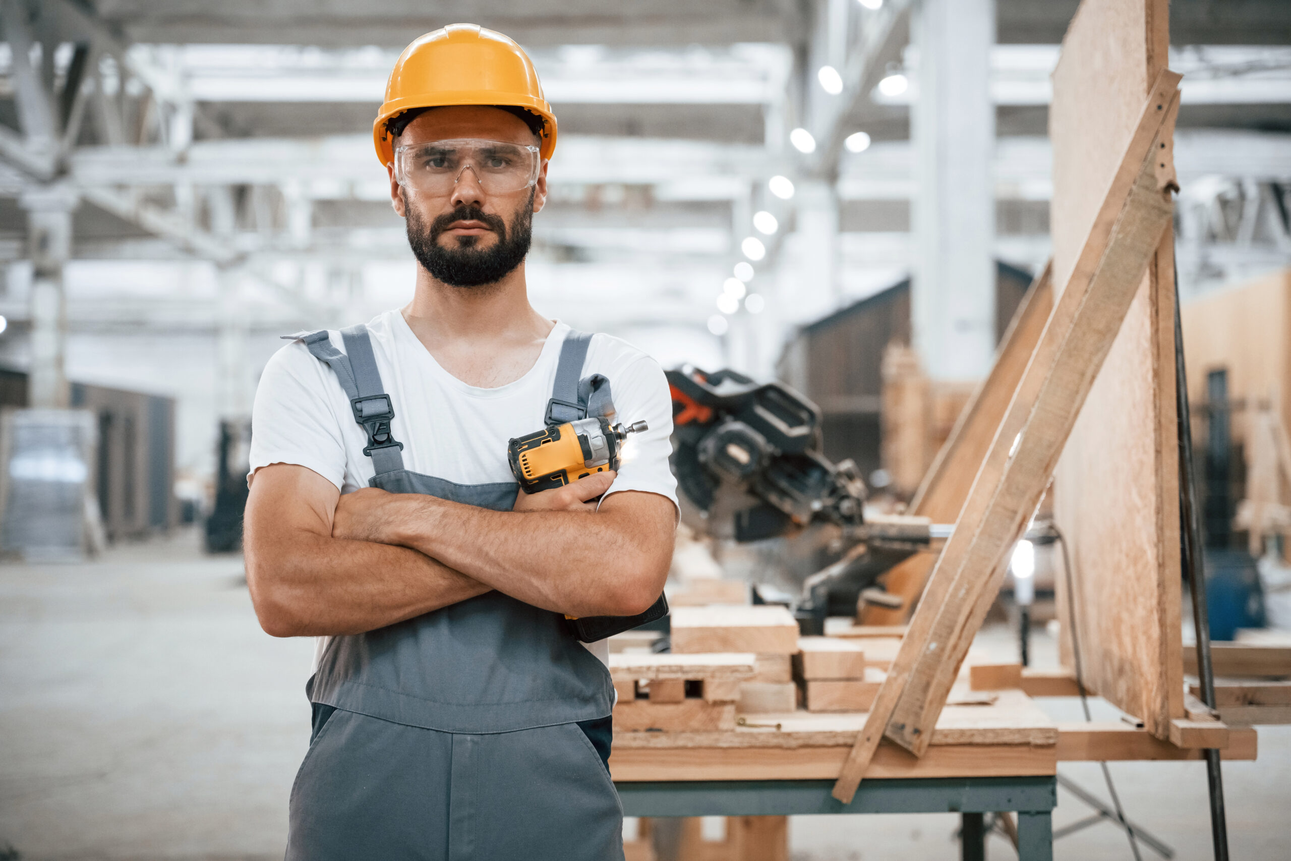 Cordless impact driver in hand. Industrial worker in wooden warehouse.