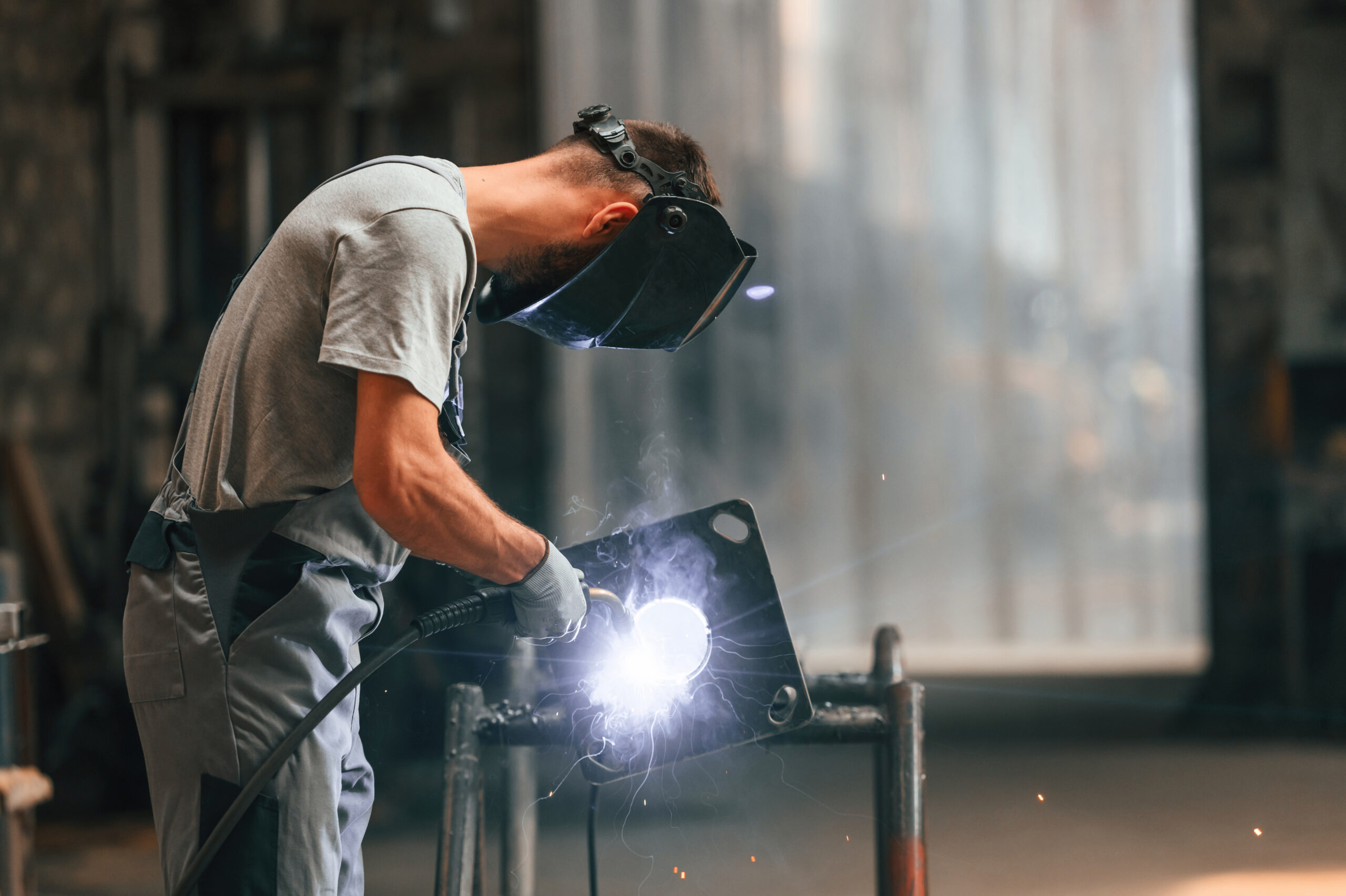 Process of welding. Young factory worker in grey uniform.