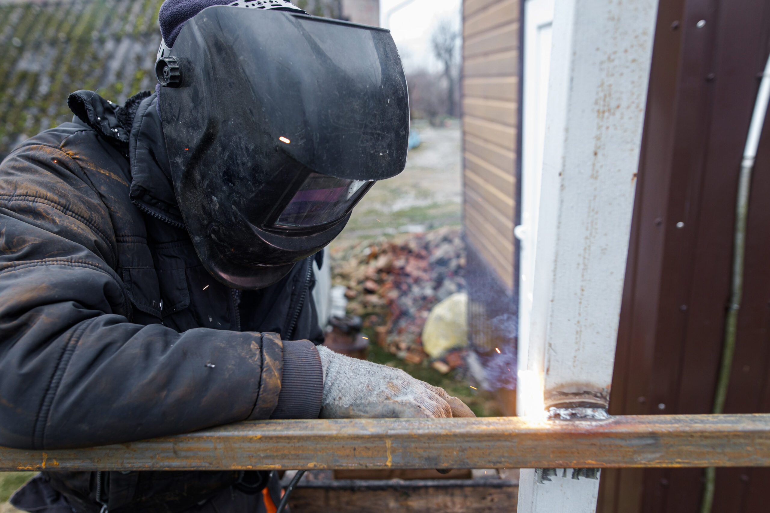 Welder man welding metal iron with electrodes, worker wearing protective helmet and gloves. Close up of electrode welding and electric sparks. Shielded metal arc welding